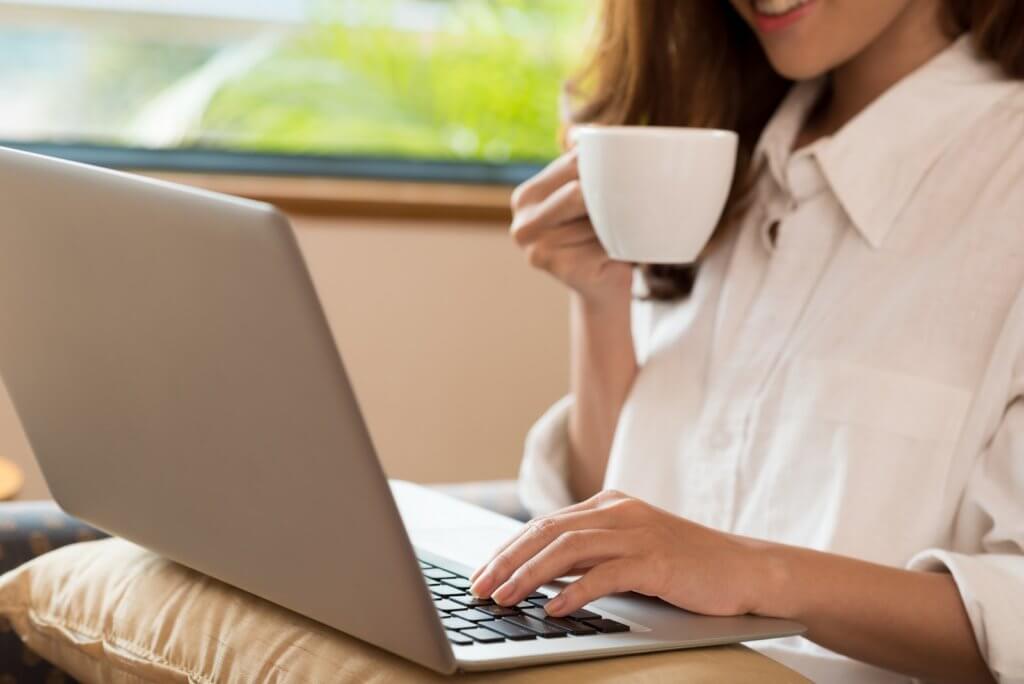 Close-up of woman drinking coffee while using laptop